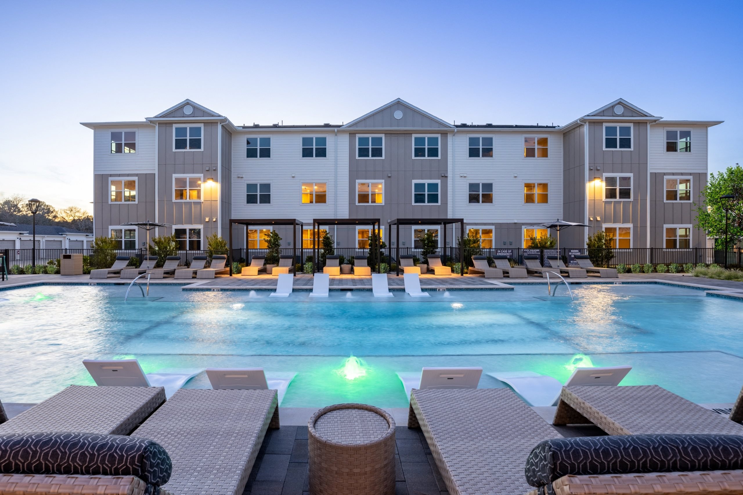 a large swimming pool with lounge chairs in front of an apartment building